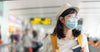 smiling-young-female-traveler-wearing-mask-with-yellow-backpack-at-the-airport-departure-hall